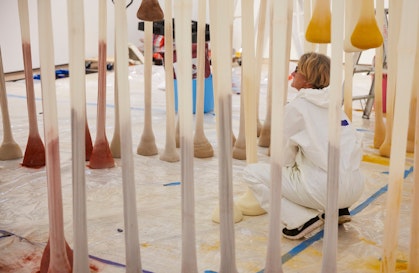 Person squats among multiple vertical fabric tubes with coloured powder pooled at the base of each tube.