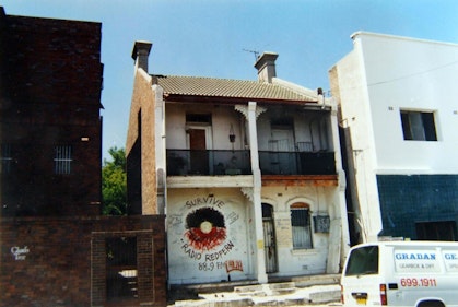 Terrace house in a row of buildings, with a stylised Aboriginal flag painted on the front and the words 'Survive' above and 'Radio Redfern 88.9 FM' below.