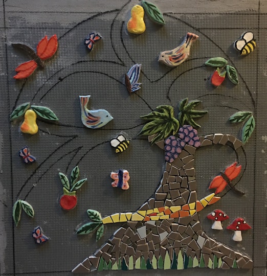 A partly constructed mosaic featuring a tree, fruit, vegetables, insects and birds.
