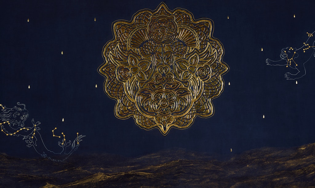 An ornate gold circular object on a dark blue background above a brown landscape. On the blue are other flecks of gold and two animal figures with gold star-like points, like zodiac animals..