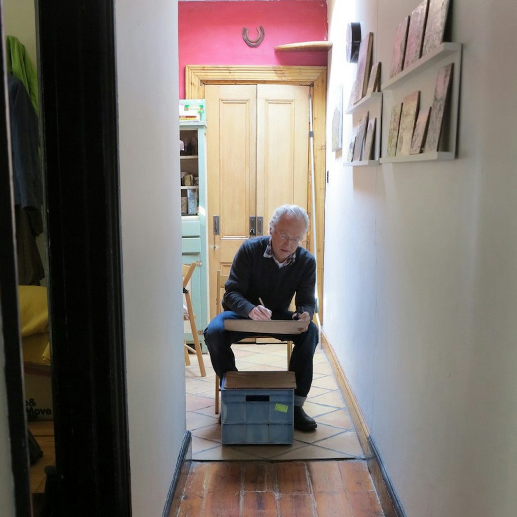 A person seated in the hallway of a home, drawing.