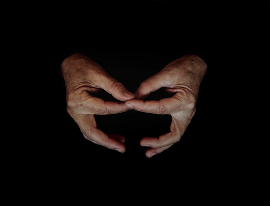 Against a dark background, two hands are positioned with the thumbs and forefingers touching.