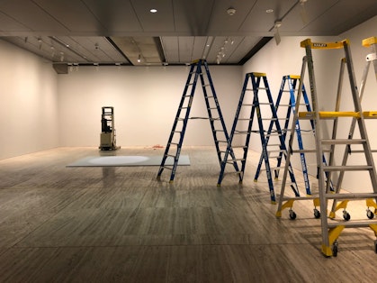 Five ladders and a forklit stand in an empty gallery space.