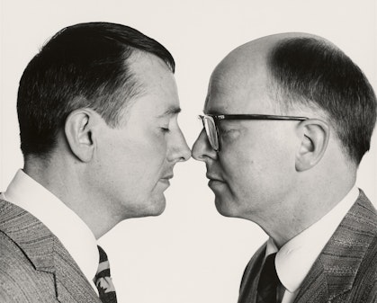 Black-and-white photo of two people facing each other, their eyes closed, the tips of their noses touching.