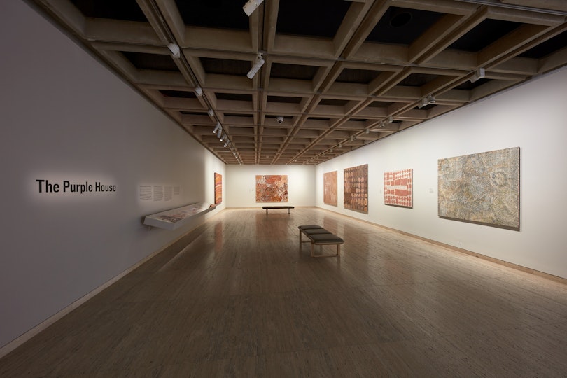 A gallery space hung with six Aboriginal paintings with 'The Purple House' written one one wall.