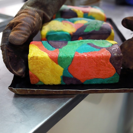 Gloved hands hold one of three multi-coloured loaves on a metal tray.