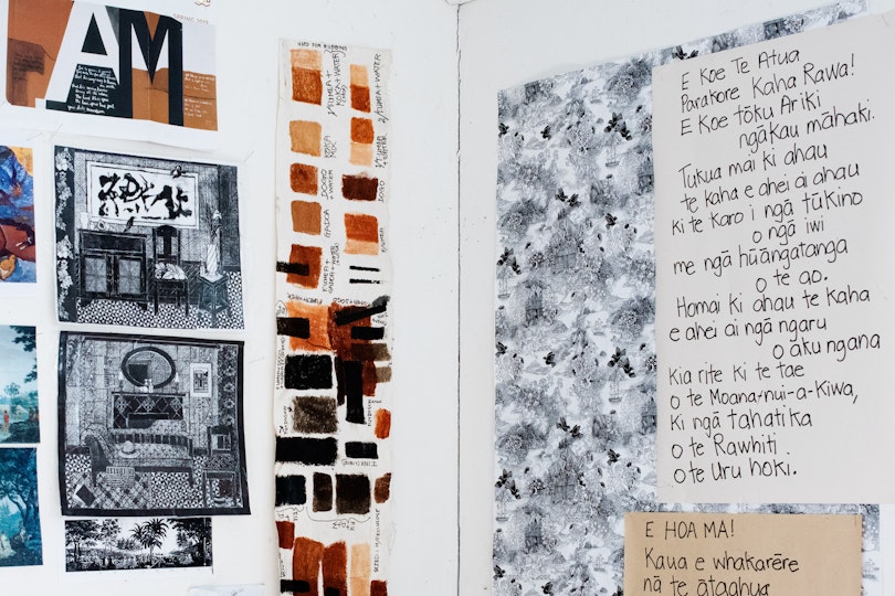 The junction of two walls, hung with multiple artwork images and sheets of paper with Maori text.