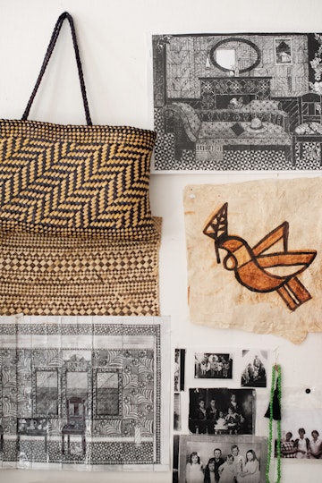 Artwork images, black-and-white photos of people, and a woven bag hang on a wall.