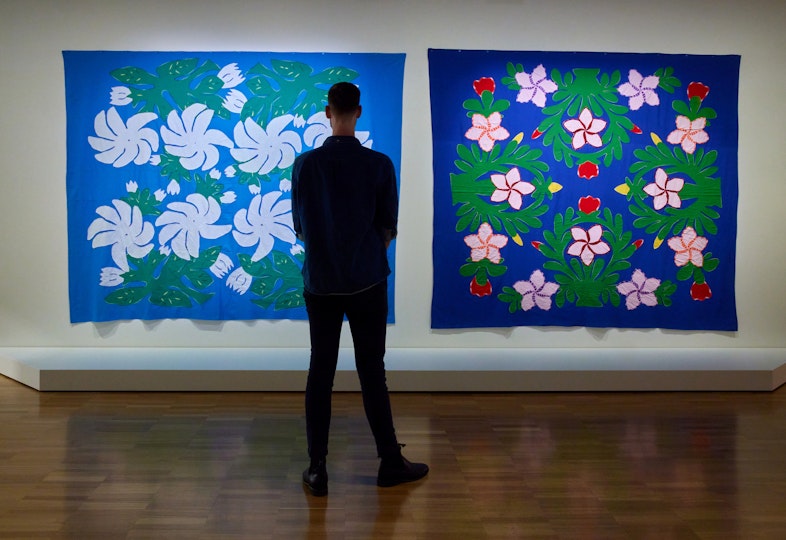 A person stands in front of two colourful fabric artworks hanging on a gallery wall.