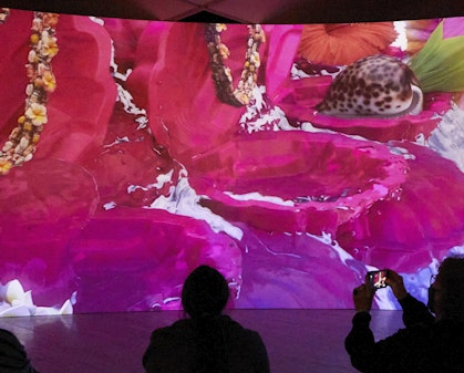 Three people sit in front of a large screen showing a brightly coloured artwork.