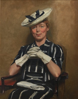 Seated woman wearing a striped black-and-white outfit and ribboned hat with her gloved hands clasped and a clutch bag on her lap