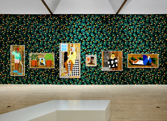 Six colourful portraits hang on a dark wall patterned with yellow and green in a gallery space.