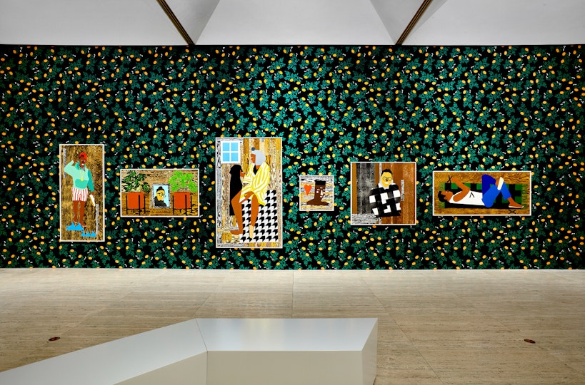 Six colourful portraits hang on a dark wall patterned with yellow and green in a gallery space.