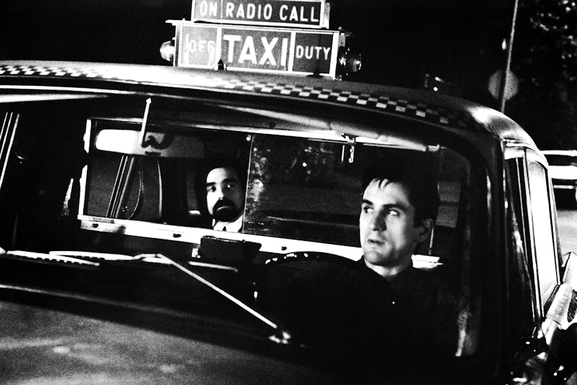 Two men sitting in a New York taxi. The driver is looking in the rear-view mirror at the passenger.