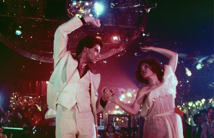 Two people dancing are looking into each others eyes. Above them is a glittering disco ball.