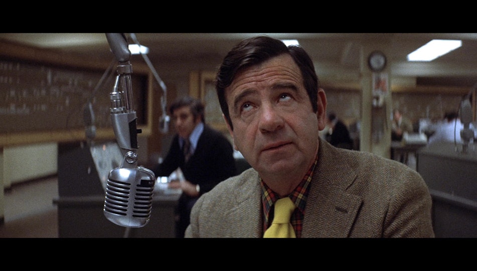 A person wit hlight skin wearing a yellow necktie looks up. In front of them is a microphone.