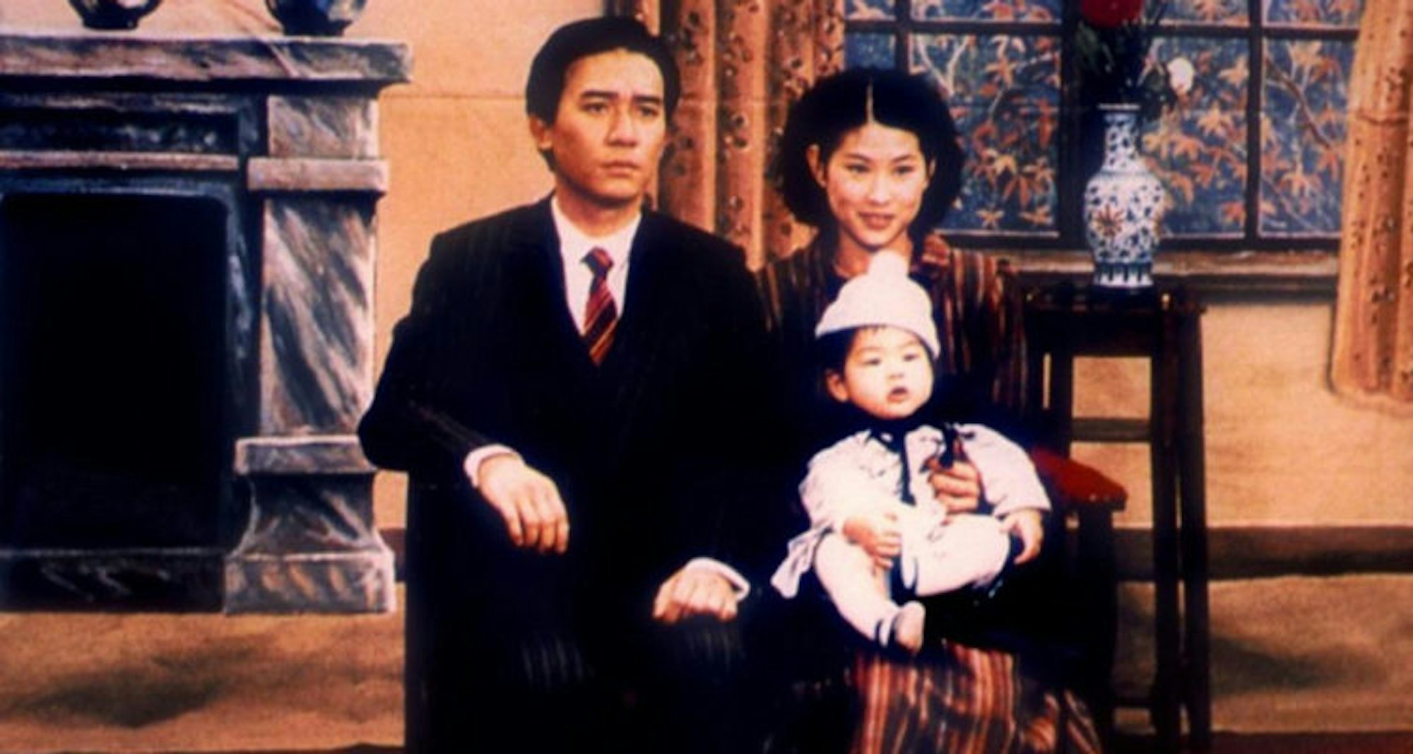 A finely dressed man and a woman with a baby on her lap are seated on a bench, posing for a family photo.