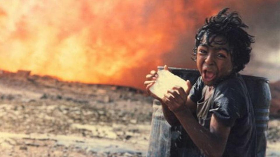 A child with black hair and medium brown skin is screaming. Behind the child is an enormous fire.