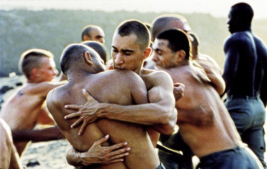 Seven shirtless people embracing one another.