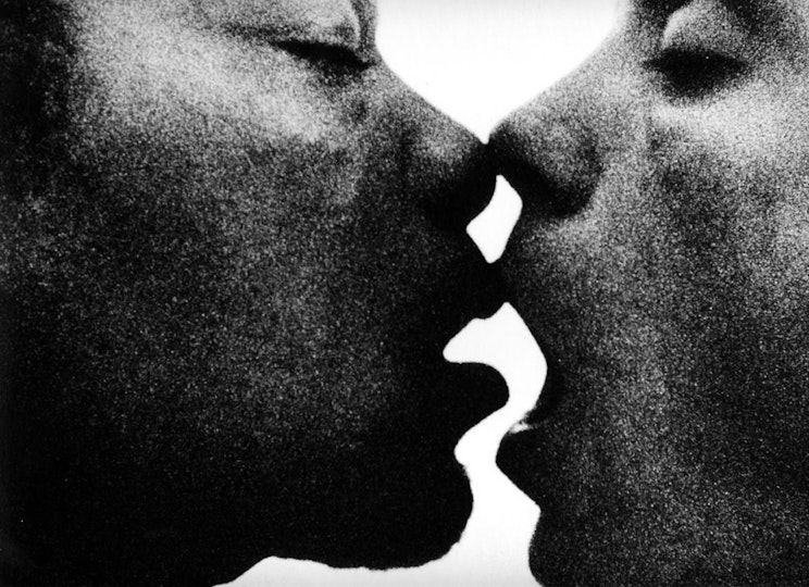 A grainy close-up of two people with their eyes closed, mouths agape and mid-kiss.