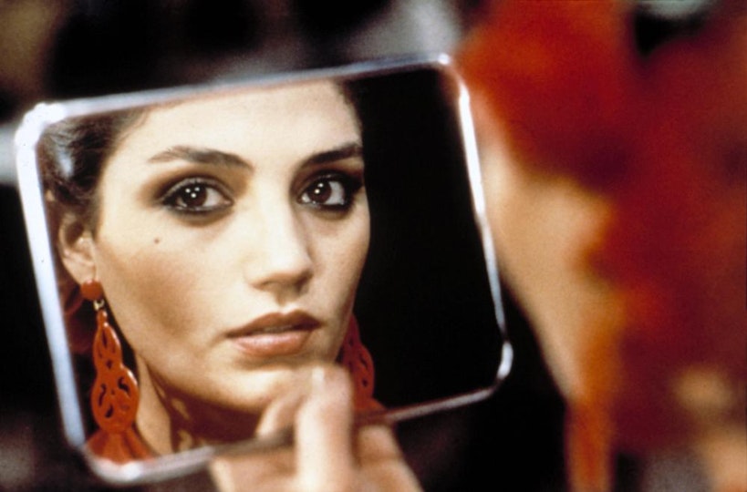 A person's face is reflected in a mirror they are holding so that the person is almost gazing into the camera.
