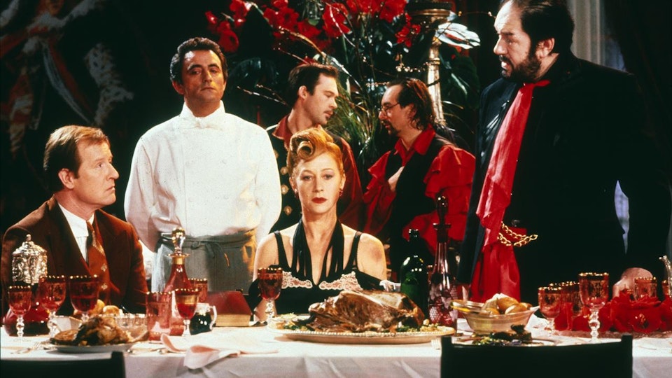Six people are at a feast-laden table. Some are looking at the camera, others are conversing in the background.