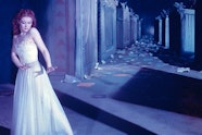 A light skinned woman in a ballet dress and red pointe shoes dances in front of a set strewn with pieces of paper and shadows.
