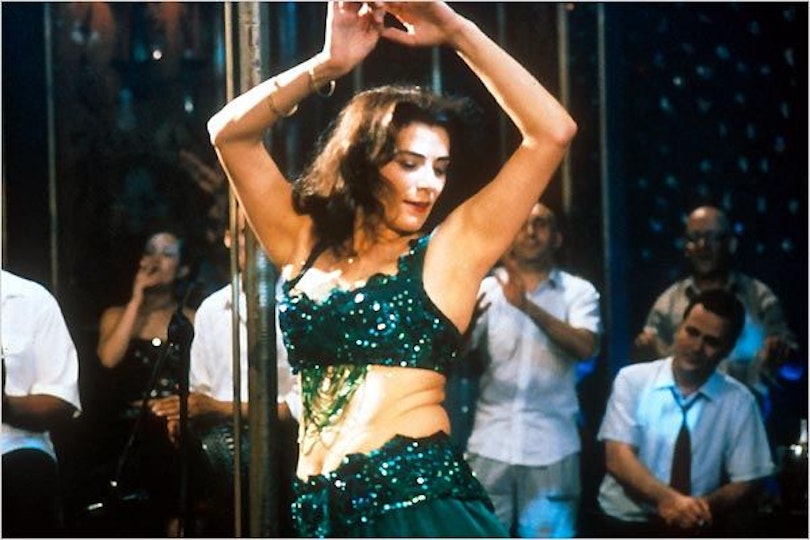A woman in a sparkling dark green top and skirt dances as people look on.