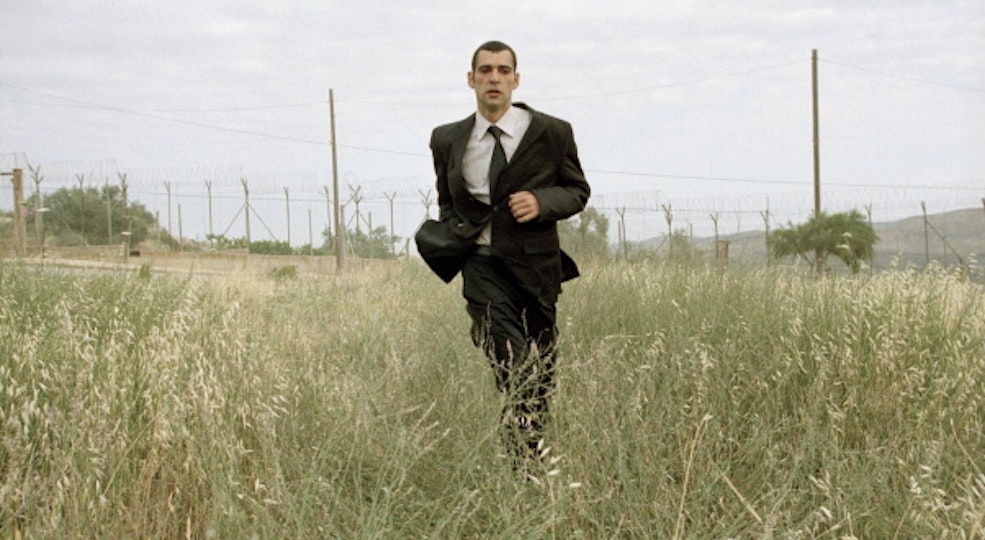A person in a suit is running through a field of long grass.