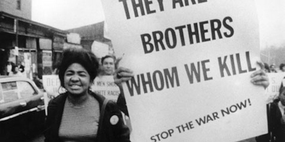 A person with medium dark skin marches next to someone holding up a protest placard. The placard reads 'They are brothers whom we kill. Stop the war now!'