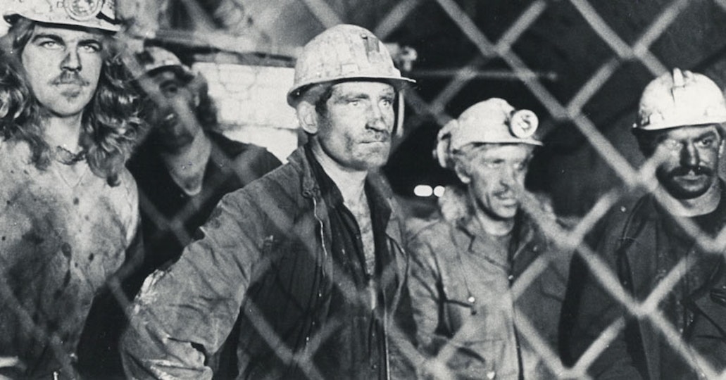 Five workers wearing hard hats gaze at something to the right of the frame.