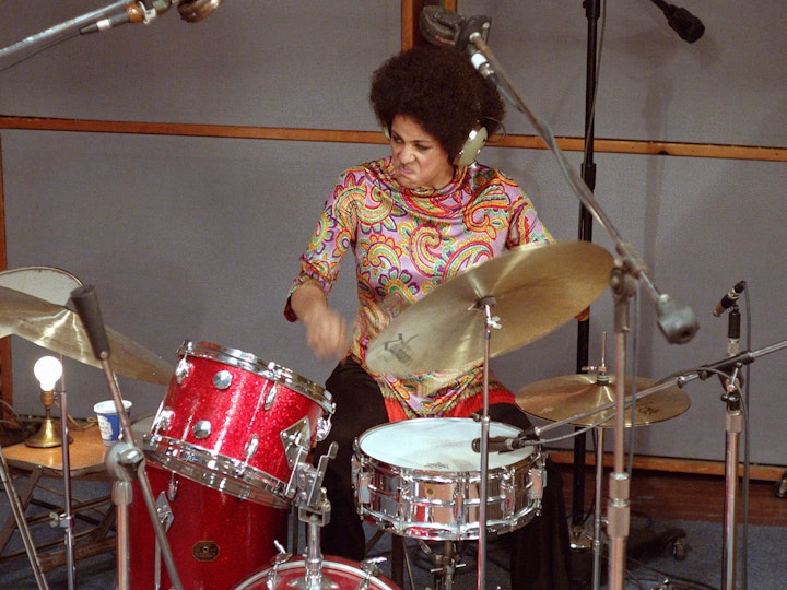 A person in a colourful paisley top plays drums.