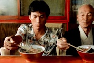 Two people with light brown skin placing chopsticks into bowls of ramen. The person on the left is frowning.