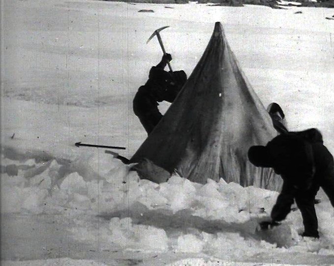 Two people dig in the snow next to a tent.