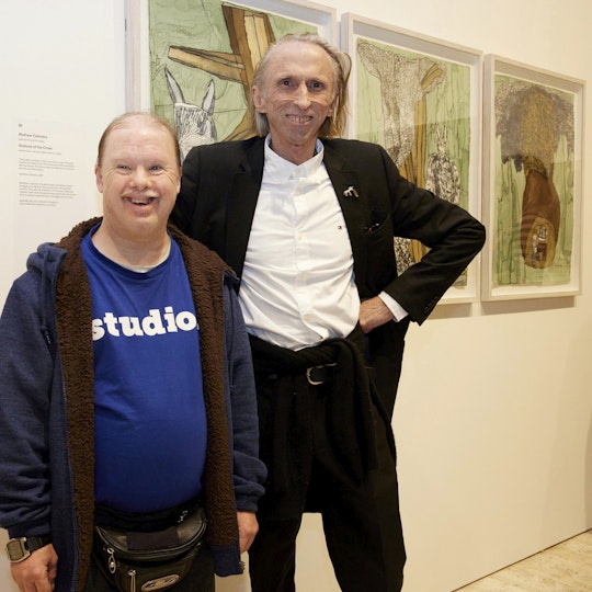 Two people stand in front of a triptych hanging on a gallery wall.