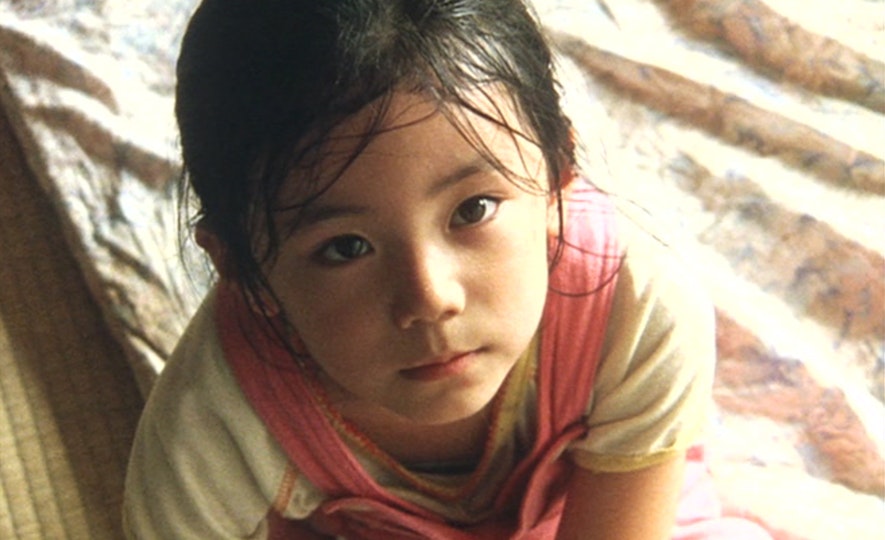 A child with damp black hair and light brown skin looks up.