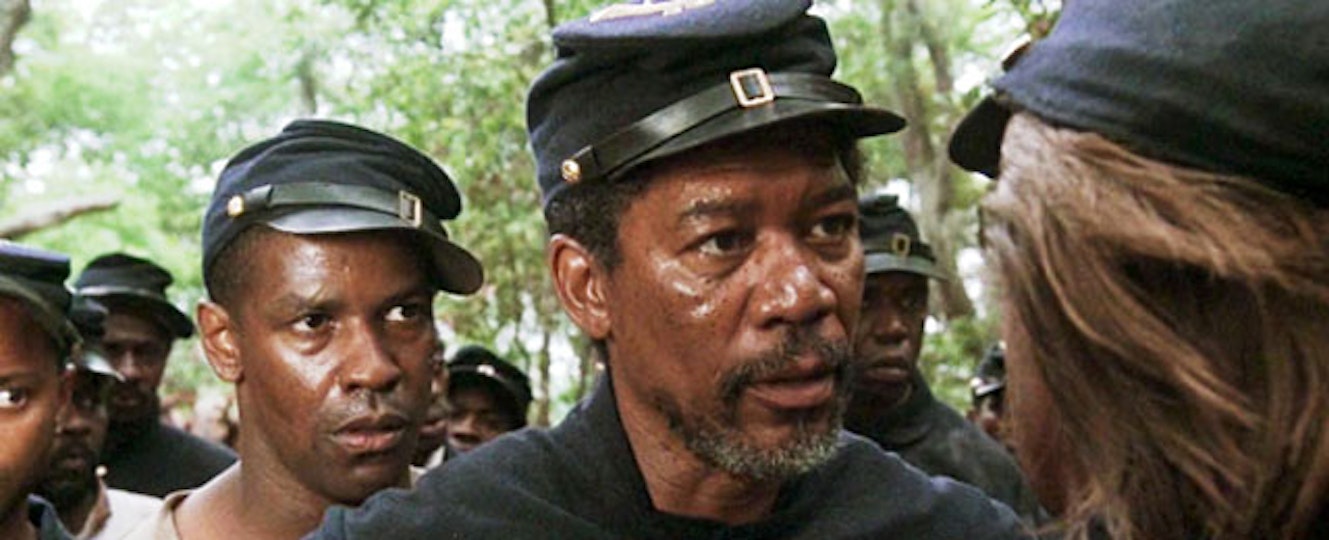 Severl people with dark brown skin wearing train driver caps look at someone whose back is to the camera. 