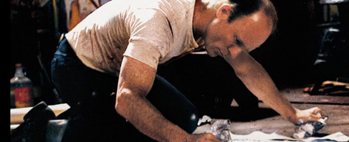 A man with light skin wearing a white t-shirt and jeans is kneeling on the floor.