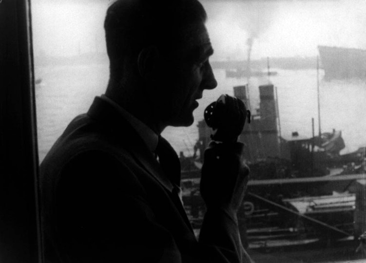 A silhouette of a person in profile holding a receiver. Behind them is a harbour with steam ships.