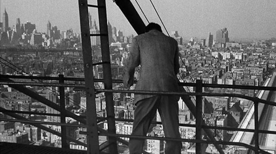 A person in a suit viewed from behind. They are standing on a scaffold next to a ladder, high above a cityscape.