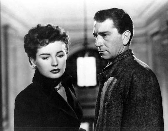 Two people standing opposite one another. The person on the right looks at the person on the left, who is looking away.