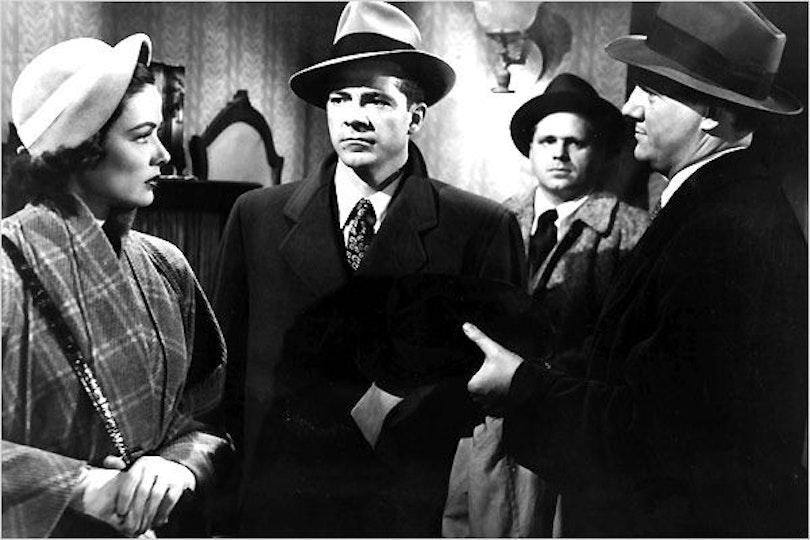 Four people wearing hats and coats looking at each other. A person on the right is holding something out to the person in the middle.