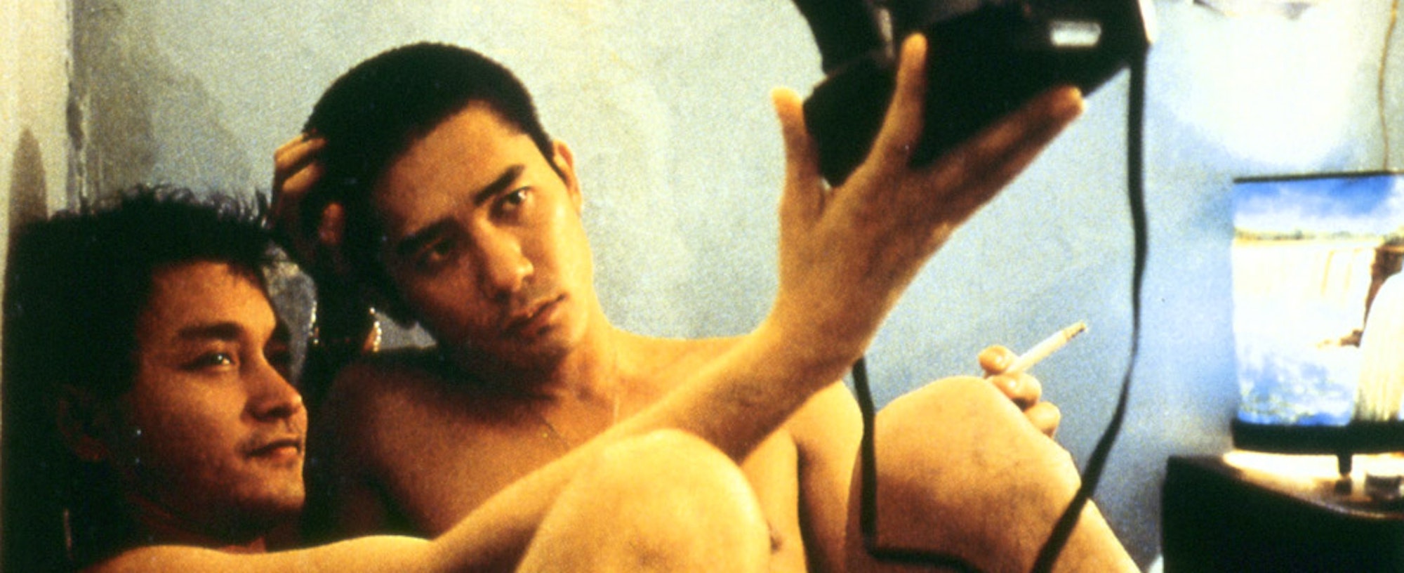 Two shirtless people with short black hair take a selfie with a film camera.
