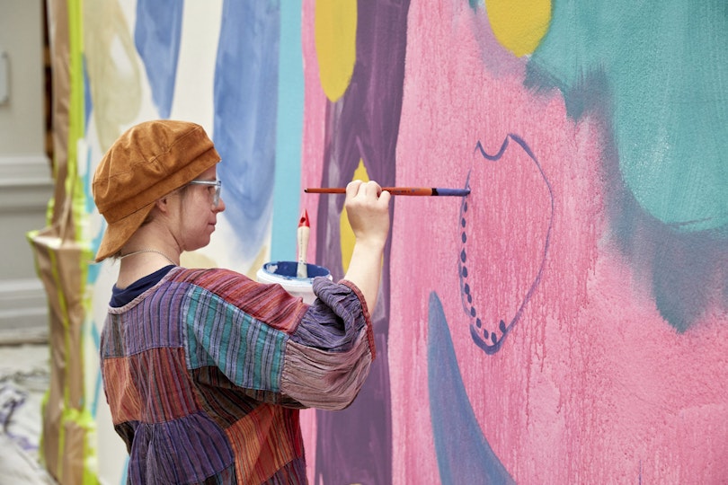 A person paints large dots within a circular shape on a wall.