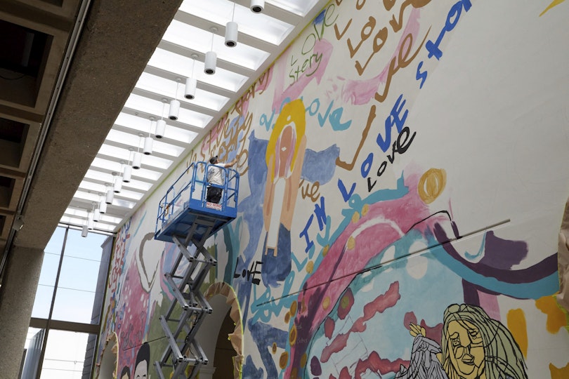 A person on a scissor lift paints the upper part of a wall, just under a high ceiling.