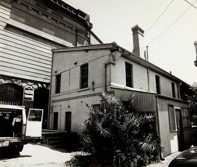 A small two-storey building with a chimney next to a much larger edifice.