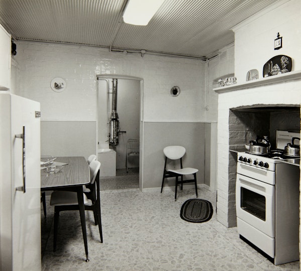 A fluorescent-lit kitchen with a freestanding oven and stove, a fridge and a dining table with chairs.