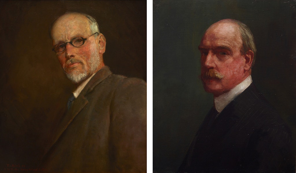 Two balding men dressed in dark jackets and white shirts. The person on the left has glasses and a cropped beard. The person on the right has a luxuriant moustache.