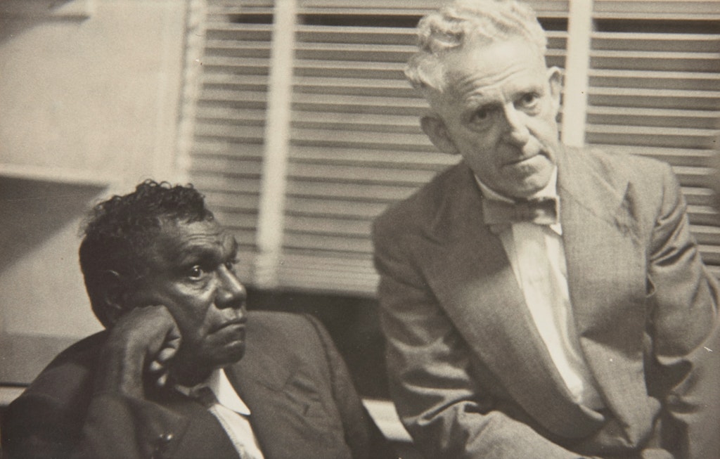 Two seated men dressed in suits. The person on the left is dark-skinned. The other is light-skinned.
