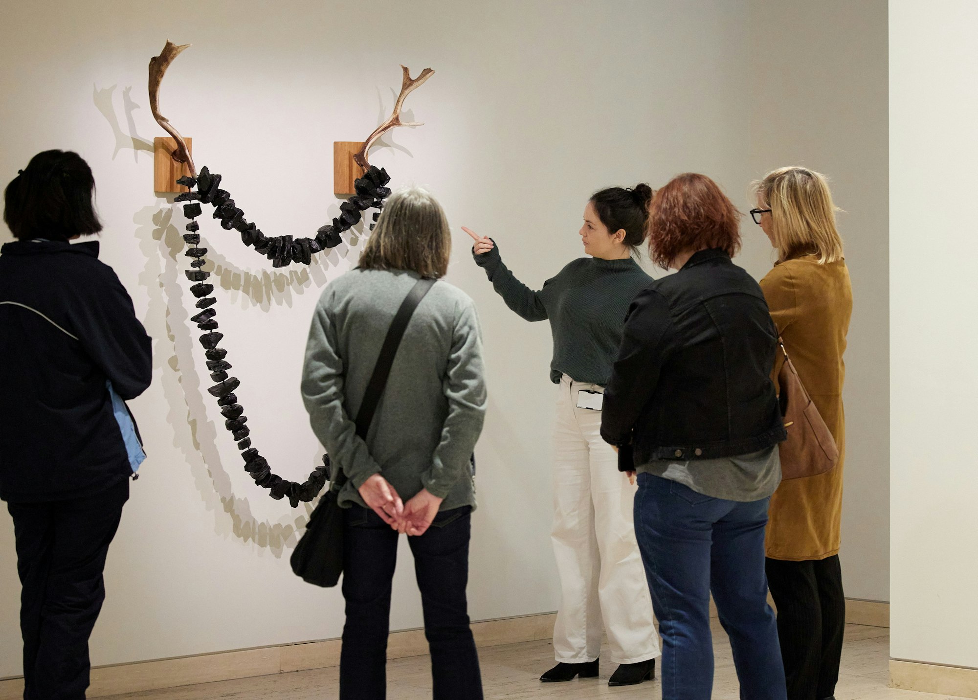 A guide leading a tour with 4 visitors and talking about the artwork 'Dark Valley, Van Diemen’s Land' by Julie Gough.